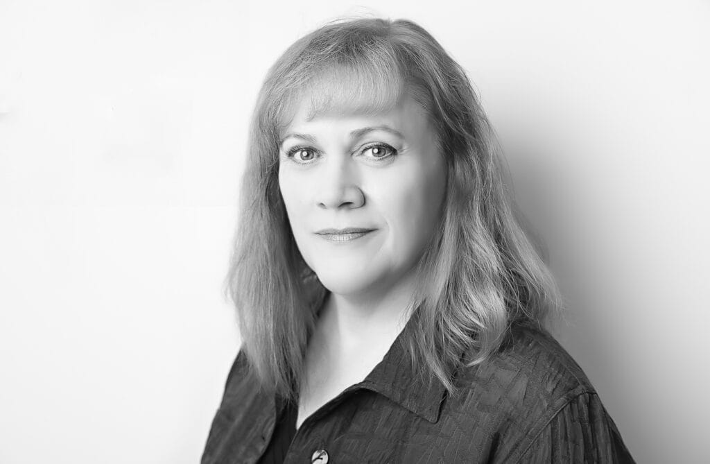 A grayscale portrait perfect for Author Headshots, featuring a woman with shoulder-length hair in a dark button-up shirt, looking directly at the camera with a neutral expression—an elegant style favored by Calgary Photographers. - Jodi O Photography
