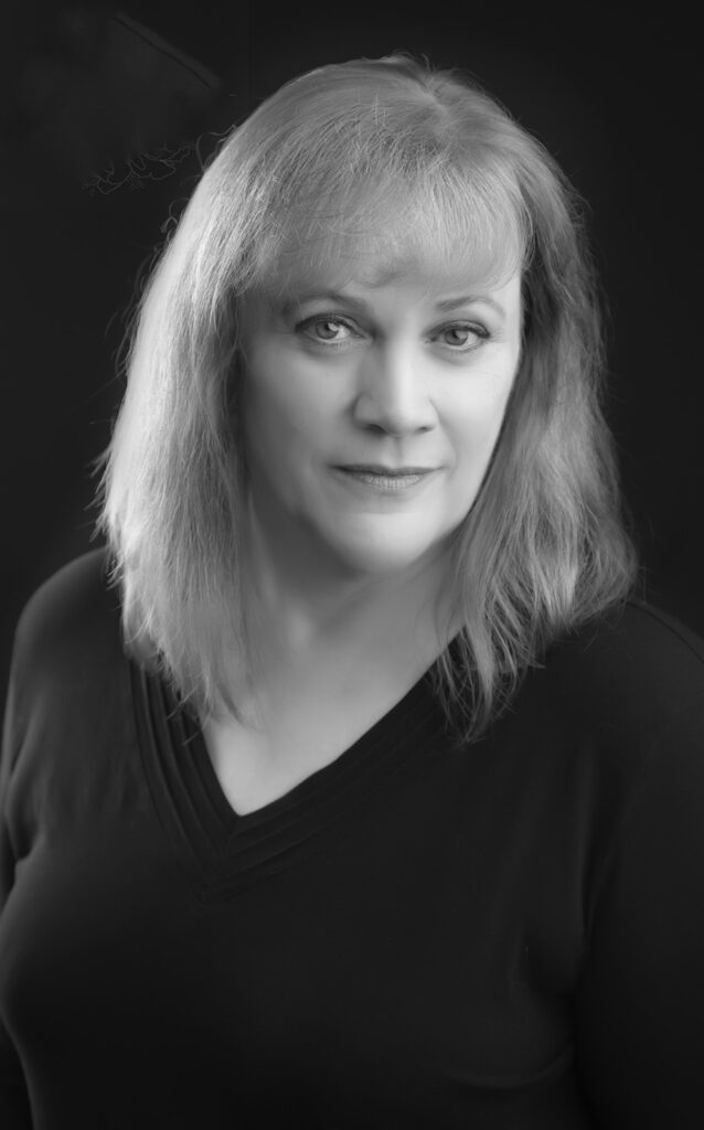Black and white headshot photography of a woman with light shoulder-length hair, wearing a V-neck dark top, gazing neutrally at the camera against a dark background—ideal for author headshots by Calgary photographers. - Jodi O Photography