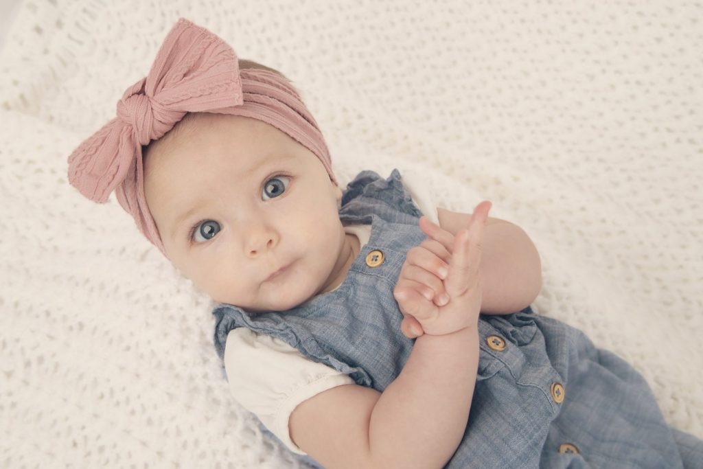 Baby girl on a vintage white blanket with blue jean outfit and pink headband