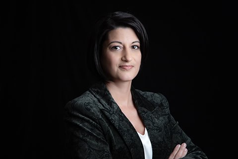 A woman with short dark hair wearing a patterned dark blazer and white top poses confidently with arms crossed against a black background, perfect for professional headshots or branding in Calgary. - Jodi O Photography