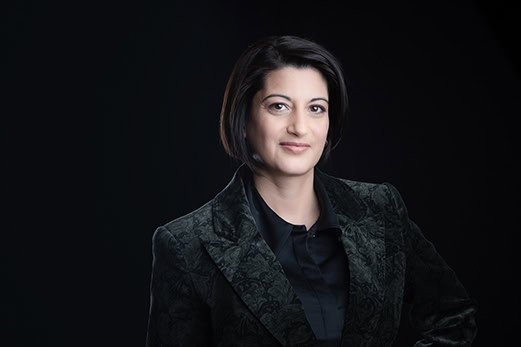 A woman with short dark hair and a slight smile wears a dark patterned blazer over a black shirt, posing against a dark background—an ideal choice for professional headshots or personal branding. - Jodi O Photography