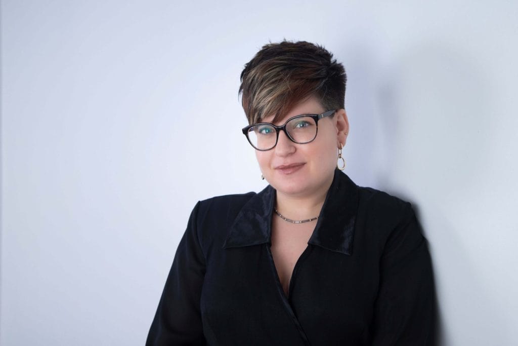 Calgary professional headshot of woman with short hair and glasses in a black suit against a white backdrop