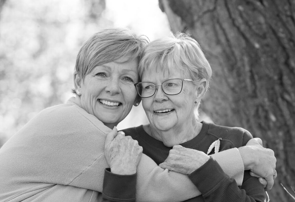 Smiling mother and daughter share a hug in a generational portrait in black and white.