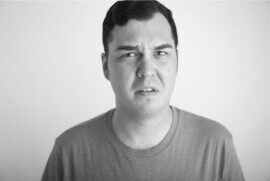 A person with short dark hair wearing a plain T-shirt stands against a blank background, displaying a confused or uncertain facial expression—ideal for actor headshots Calgary clients might seek. - Jodi O Photography