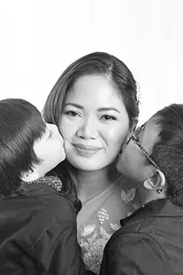 A woman smiles while being kissed on each cheek by two young children in this heartwarming black and white family photo taken in Calgary. - Jodi O Photography