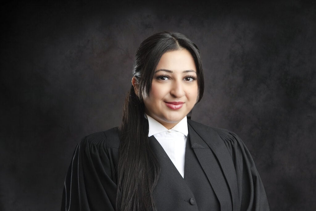 A woman with long dark hair, wearing a black judge or lawyer robe and a white shirt, poses confidently against a dark, textured background. - Jodi O Photography
